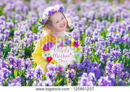 Child playing in hyacinth field. Little girl holding a wooden heart shape chalk board standing in a park with spring hyacinths flowers. Copy space for your text. Happy mother's day card.