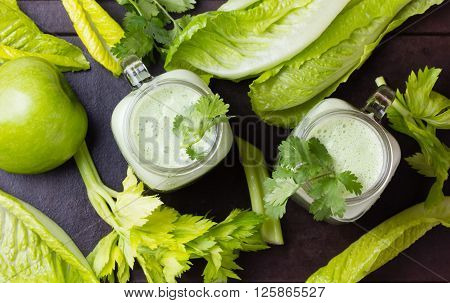 Two glasses of green smoothie and fresh green vegetables and fruits on black background. Top view