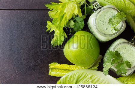 Two glasses of green smoothie and fresh green vegetables and fruits on black background. Top view