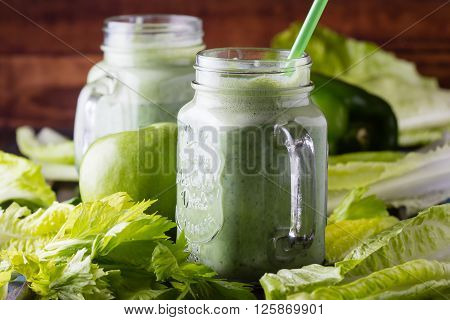 Two glasses of green smoothie and fresh green vegetables and fruits on wooden blue background