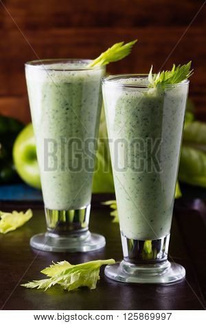 Two glasses of green smoothie and fresh green vegetables and fruits on black background