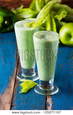 Two glasses of green smoothie and fresh green vegetables and fruits on wooden blue background