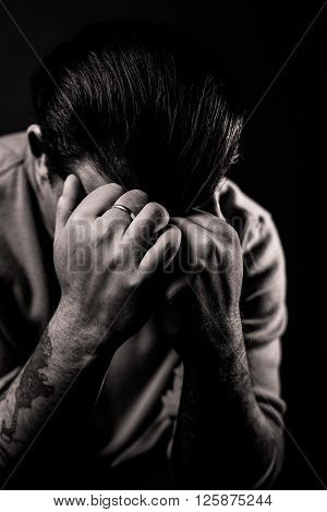 A man hides his face in angst against a black background