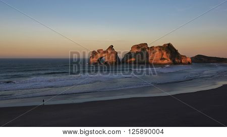 Tourist watching sunset at Wharariki Beach. Unique rock formations in New Zealand.