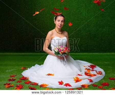 Young and beautiful bride with the flower bouquet and  falling red maple leaf the green background