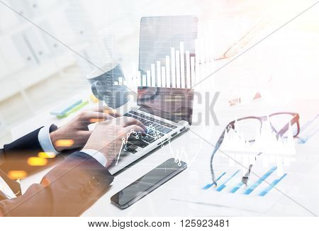 Businessman typing on laptop glasses smartphone and cup aside. Graphs and diagrams. Only hands seen. Double exposure. Concept of work.
