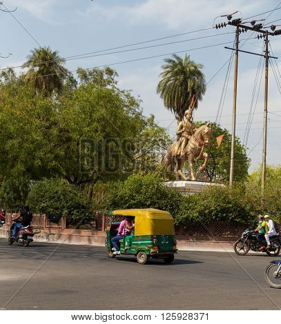 AGRA INDIA - 25TH MARCH 2016: Traffic along streets of Agra during the day. Tuk Tuk Rickshaws motorbikes and a statue can be seen.