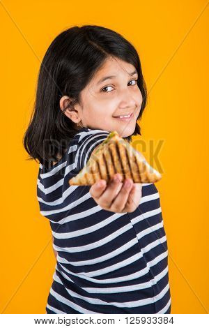 indian girl eating sandwich, asian girl and sandwich, cute indian girl posing with sandwich on yellow background