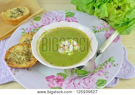 Bowl with fresh green vegetarian soup (pottage) with sour cream and pieces of garlic bread
