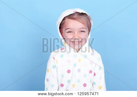 Laughing child girl 3-4 years old posing in room over blue. Wearing hoodie with polka dots. Looking at camera. Having fun.