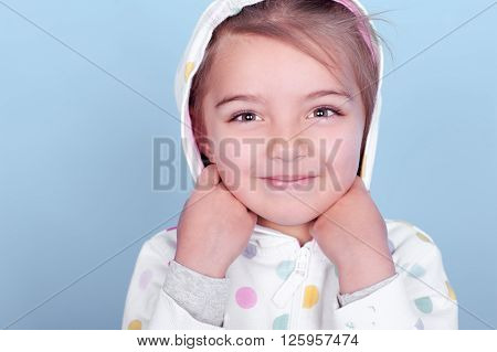 Smiling little girl wearing white hoodie with polka dots over blue. Posing in room. Looking at camera. Close up portrait.