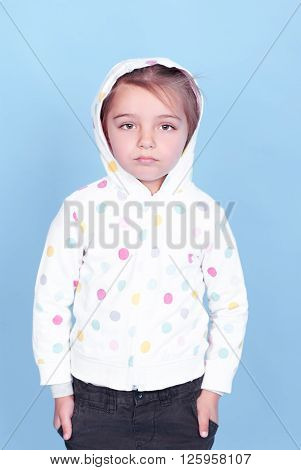 Sad kid girl 3-4 year old wearing sporty hoodie over blue. Childhood. Looking at camera.