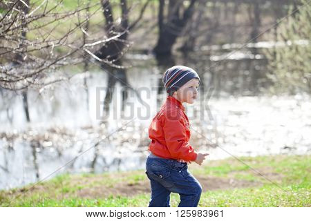 Close up portrait of a beautiful baby boy walking in spring park. Little boy in orange jaket and blue jeans, outdoors