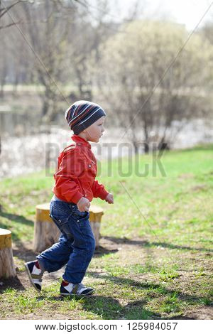 Full length portrait of a beautiful baby boy walking in spring park. Little boy in orange jaket and blue jeans, outdoors