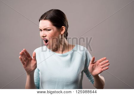 Real aversion. Pleasant emotional  cheerless girl using gesture and expressing disgust while standing isolated on grey background