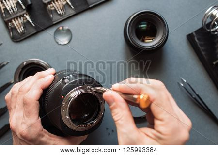 Photo camera lens repair set. Technician engineer check optics alignment and maintenance support of broken photographic 85 1.2 photo camera lens part. Pov to workshop and engineer's hands.