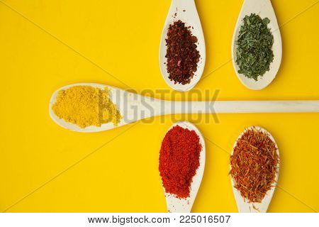 Wooden and plastic spoons with dry spices and fresh herbs on a yellow background with copy space, top view, close up