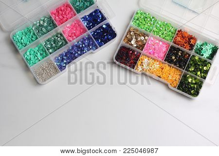plastic box with sequin of different colors. marble light background, flat lay, space for text