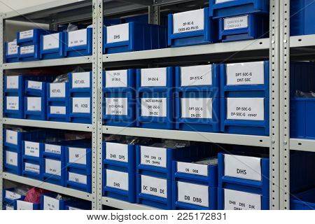 Warehouse of spare parts and components of industrial electronics. Blue plastic trays in metal racks.