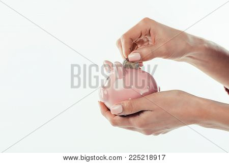 cropped view of woman putting coin into little piggy bank, isolated on white
