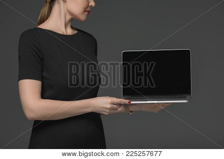cropped shot of attractive woman holding laptop with blank screen isolated on grey