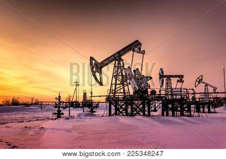 Pump jack, wellhead and pipeline during sunset in the oilfield. Winter period. Oil and gas concept. Toned.