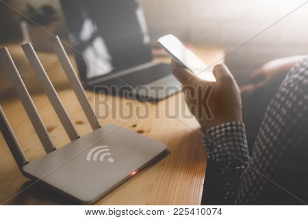 Closeup Of A Wireless Router And A Man Using Smartphone On Living Room At Home Ofiice