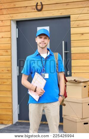Smiling delivery man in blue uniform delivering parcel box to recipient - courier service concept. Smiling delivery man in blue uniform