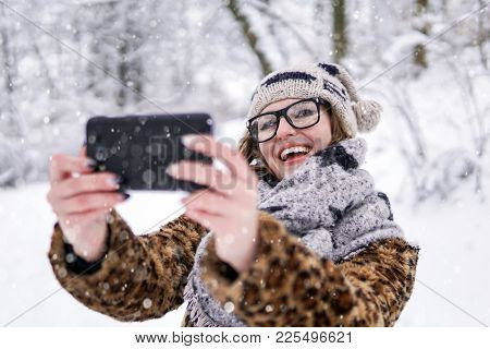 Attractive Girl Wears Glasses Making Selfie By Smartphone In Winter Snowy Park