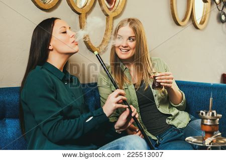 Two Happy Women Are Sitting In Shisha Bar And Smoking Nargile