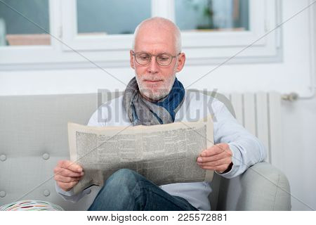 Handsome Mature Man Reading A Newpaper On Sofa