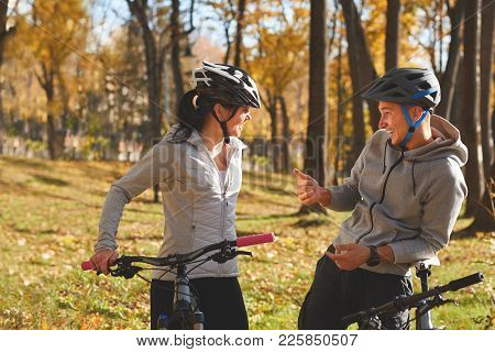 Happy Young Couple Having Fun Riding A Bicycle On Sunny Autumn Day In The Park. Two People Are Talki