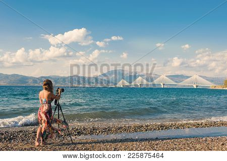 Young Female On The Beach With Tripod And Camera Taking Picture Of Rion-antirion Bridge Near Patras,