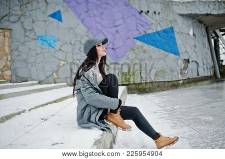 Stylish Brunette Girl In Gray Cap, Casual Street Style On Winter Day Against Colored Wall.