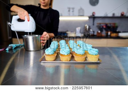 The Confectioner With A Pipping Bag Of Cream In His Hands Decoretion Cupcake On The Table In The Kit