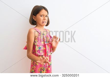 Young beautiful child girl wearing pink floral dress standing over isolated white background disgusted expression, displeased and fearful doing disgust face because aversion reaction. 