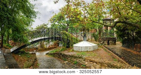 Part Of City Garden With Decorative Bridge, Sculpture And Arbor In Rainy Autumn Day. Park Old Odesa 