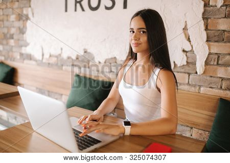 Attractive Smart Girl Working On Laptop In Cafe. Beautiful Girl Using Computer For Work. Girl Grinki