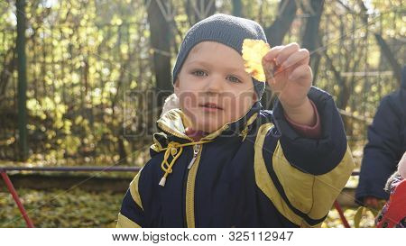 Autumn Time. Little Smiling Child With Yeallow Leaf Dressed In Black-yeallow Jacket In The Kindergar