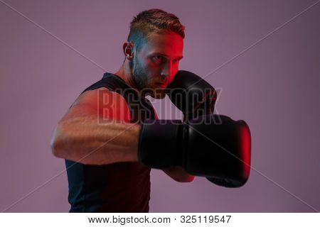 Image of a handsome strong young sports man boxer posing isolated over neon lights in gloves make boxing exercises.