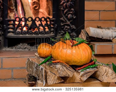 Two Halloween Pumpkins Lie On Birch Firewood In Front Of A Blazing Fireplace. On The Pumpkins Are Ho