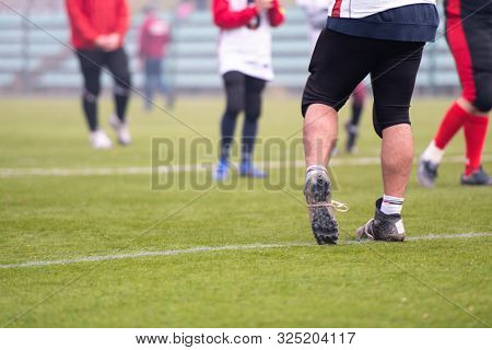 close up shot of group young professional american football players warming up and stretching together before a practice on the field  focus on the legs