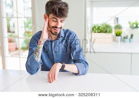 Young man wearing casual shirt sitting on white table Looking at the watch time worried, afraid of getting late