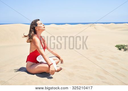 Young beautiful woman sunbathing and relaxing sitting on the sand doing yoga poses at maspalomas dunes bech