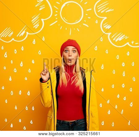 Girl Indicates The Sun Between The Clouds Above. Amazed And Shocked Expression. Yellow Background