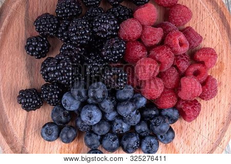 Close View On Unmixed Heaps Of Colorful Berries On Textured Wooden Plate