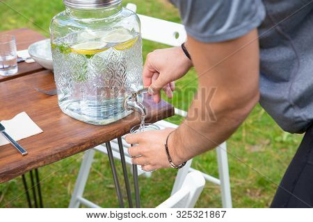 Man Pouring Lemonade In Glass. Close-up Partial View Of Young Man Holding Glass And Pouring Healthy 