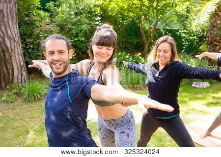 Trainer Helping Man In Yoga Practice. Smiling Young Woman Helping Cheerful Man In Yoga Practice Outd