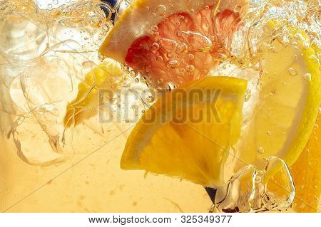 Close Up Of Lemon Slices In Stirring The Lemonade And Ice Cubes On Background. Texture Of Cooling Sw