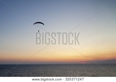 Paraglider With A Man High In The Blue Sky Against The Setting Sun.